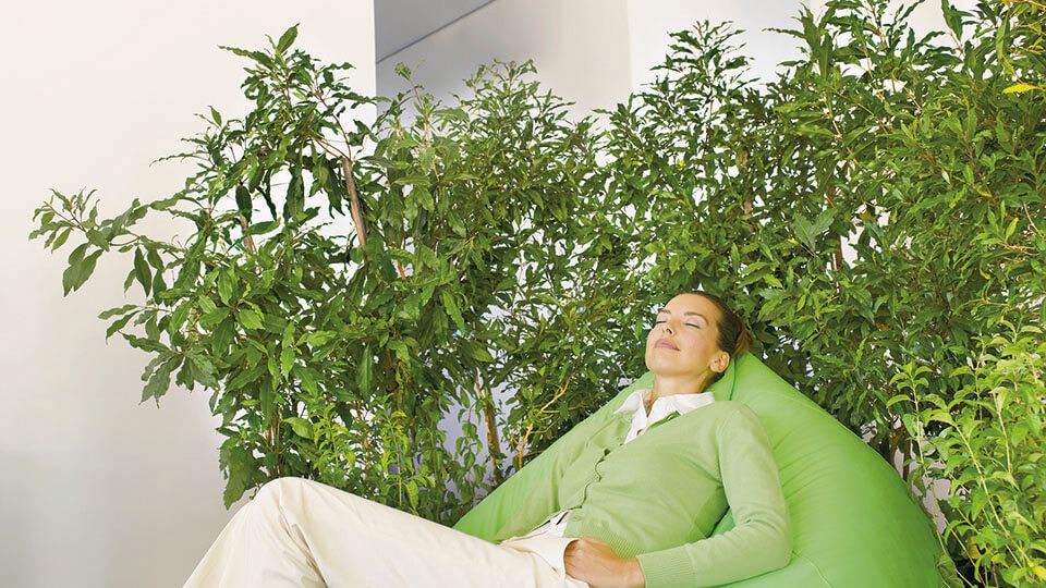 Frau entspannt in Sessel von Pflanzen umgeben